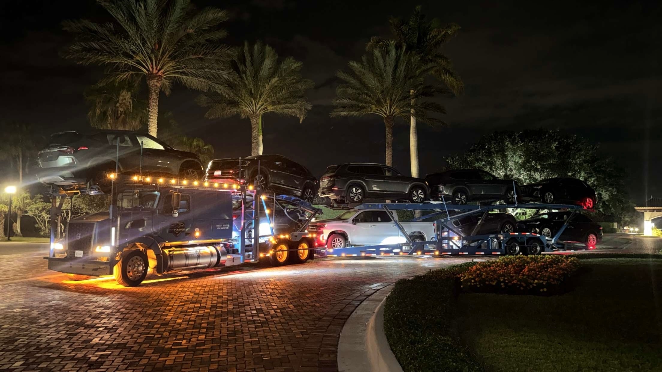 GOCARGO blue car carrier truck at night at a resort with palm trees