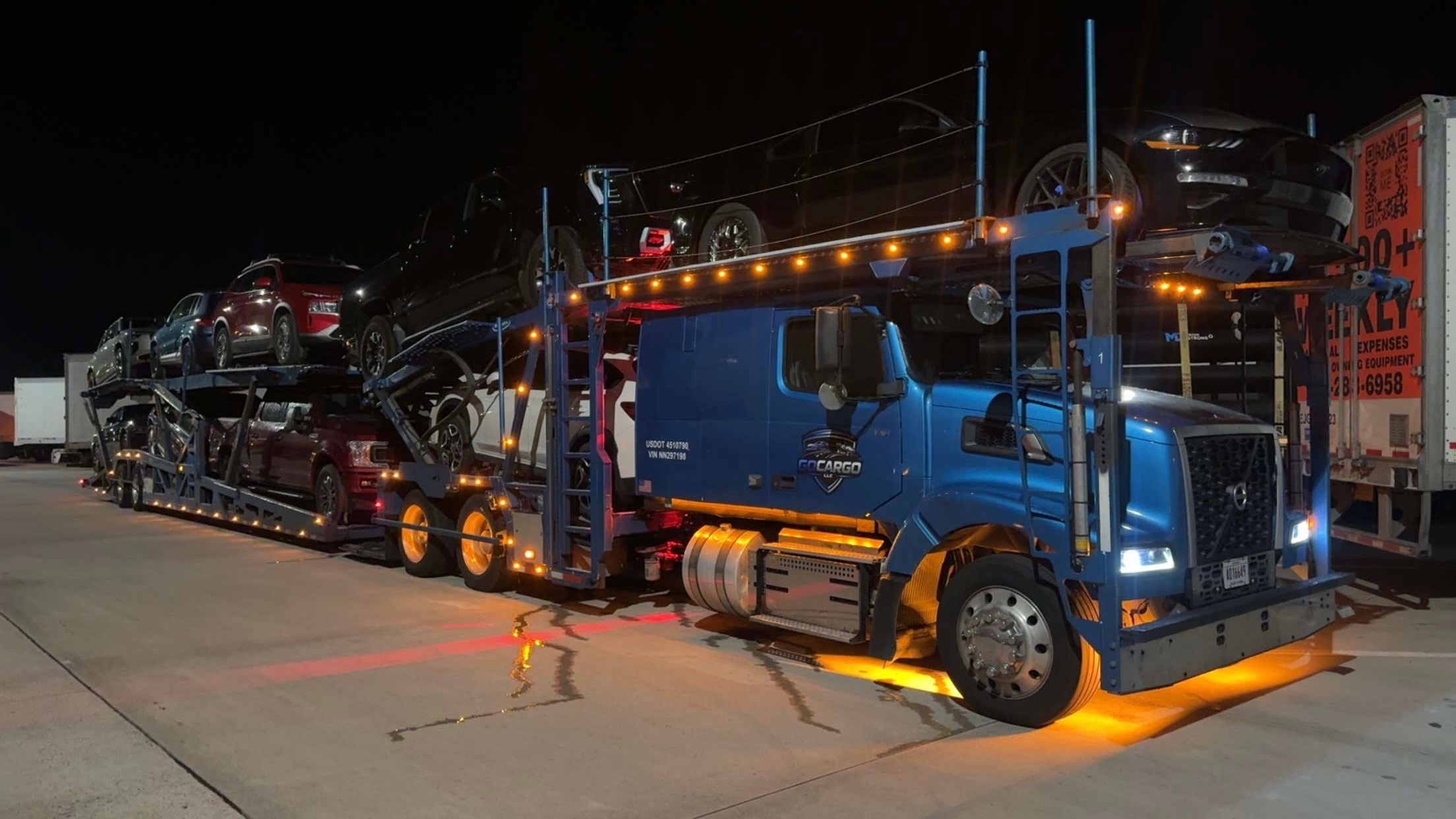 GOCARGO blue car carrier truck at night with orange underglow lighting at a truck stop