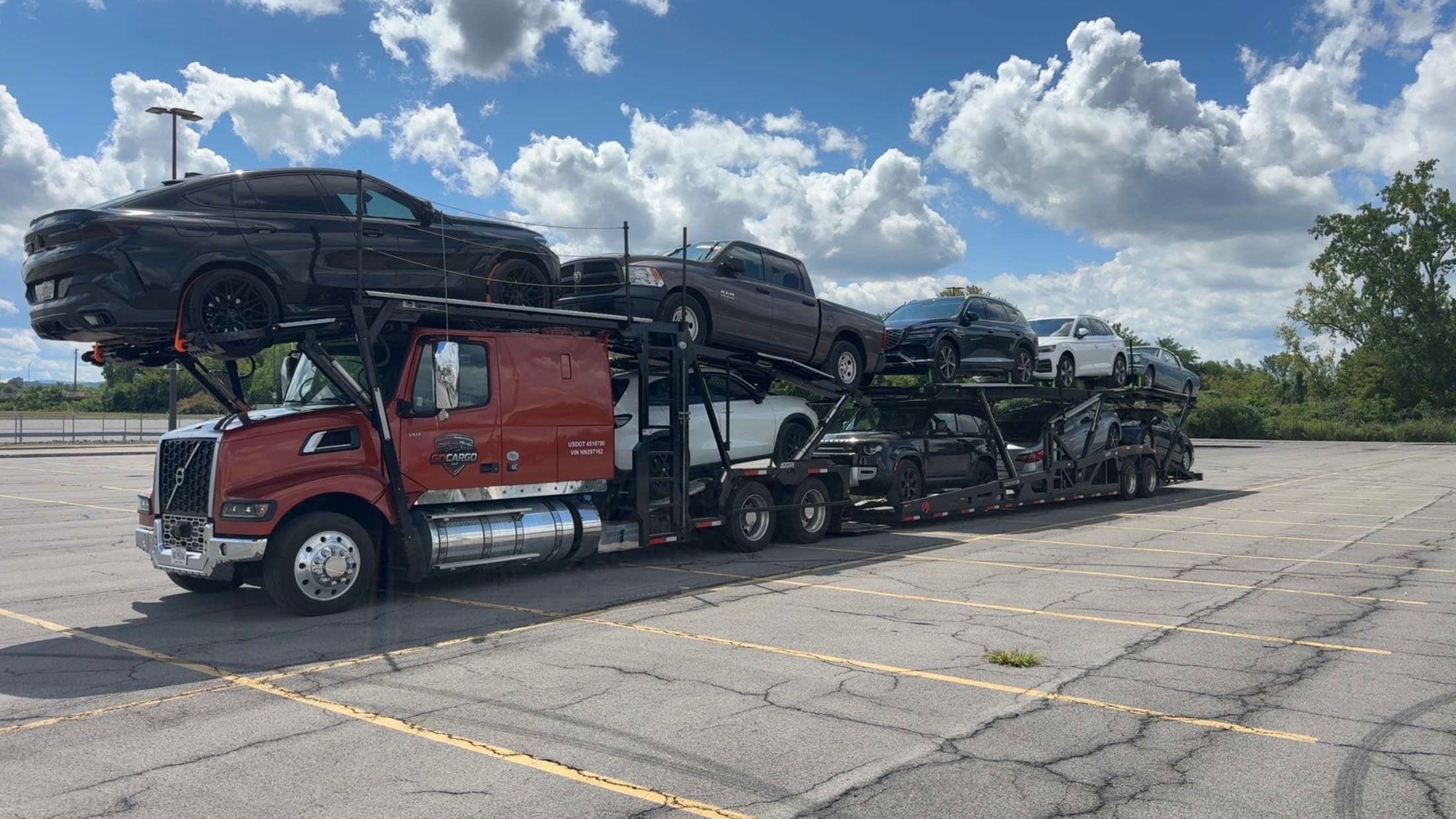 GOCARGO red car carrier truck loaded with vehicles in a parking lot on a cloudy day